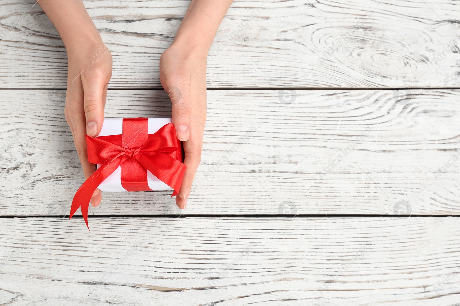 Photo of Young woman holding beautiful gift box on wooden background, top view