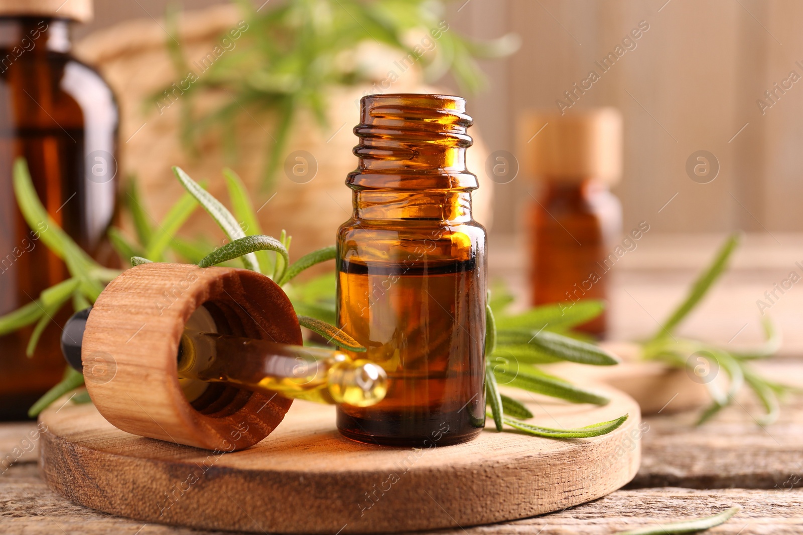 Photo of Aromatic essential oil in bottle, pipette and rosemary on wooden table, closeup