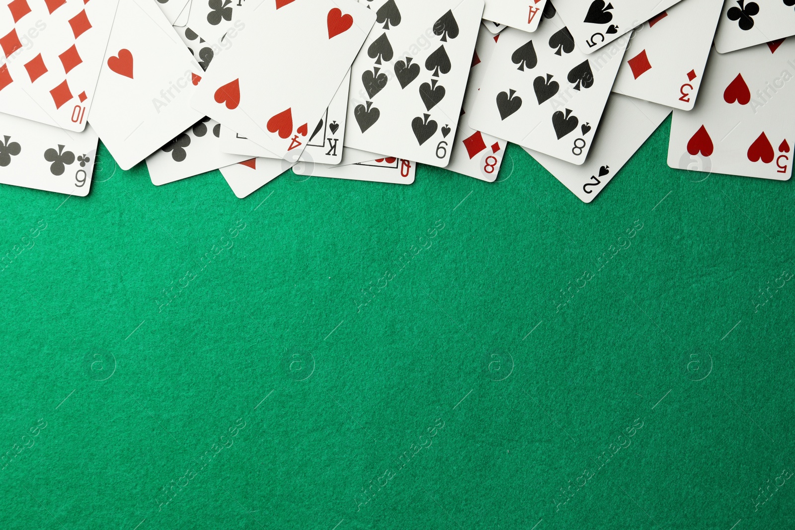 Photo of Scattered playing cards on green table, top view. Space for text