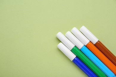 Photo of Different colorful markers on light green background, flat lay. Space for text