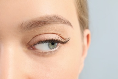 Photo of Young woman with beautiful long eyelashes on gray background, closeup. Extension procedure