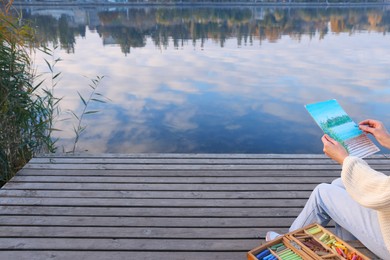 Woman drawing with soft pastels on wooden pier near river, closeup