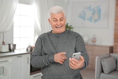 Mature man laughing while using smartphone at home