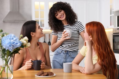 Photo of Happy young friends with cups of drink spending time together in kitchen