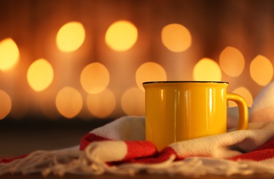 Cup of hot drink on scarf against blurred background. Winter atmosphere