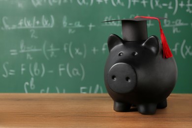 Photo of Scholarship concept. Piggy bank and graduation cap on wooden table, space for text