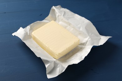 Block of tasty butter in open foil packaging on blue wooden table