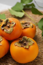 Photo of Delicious ripe juicy persimmons on wicker mat, closeup