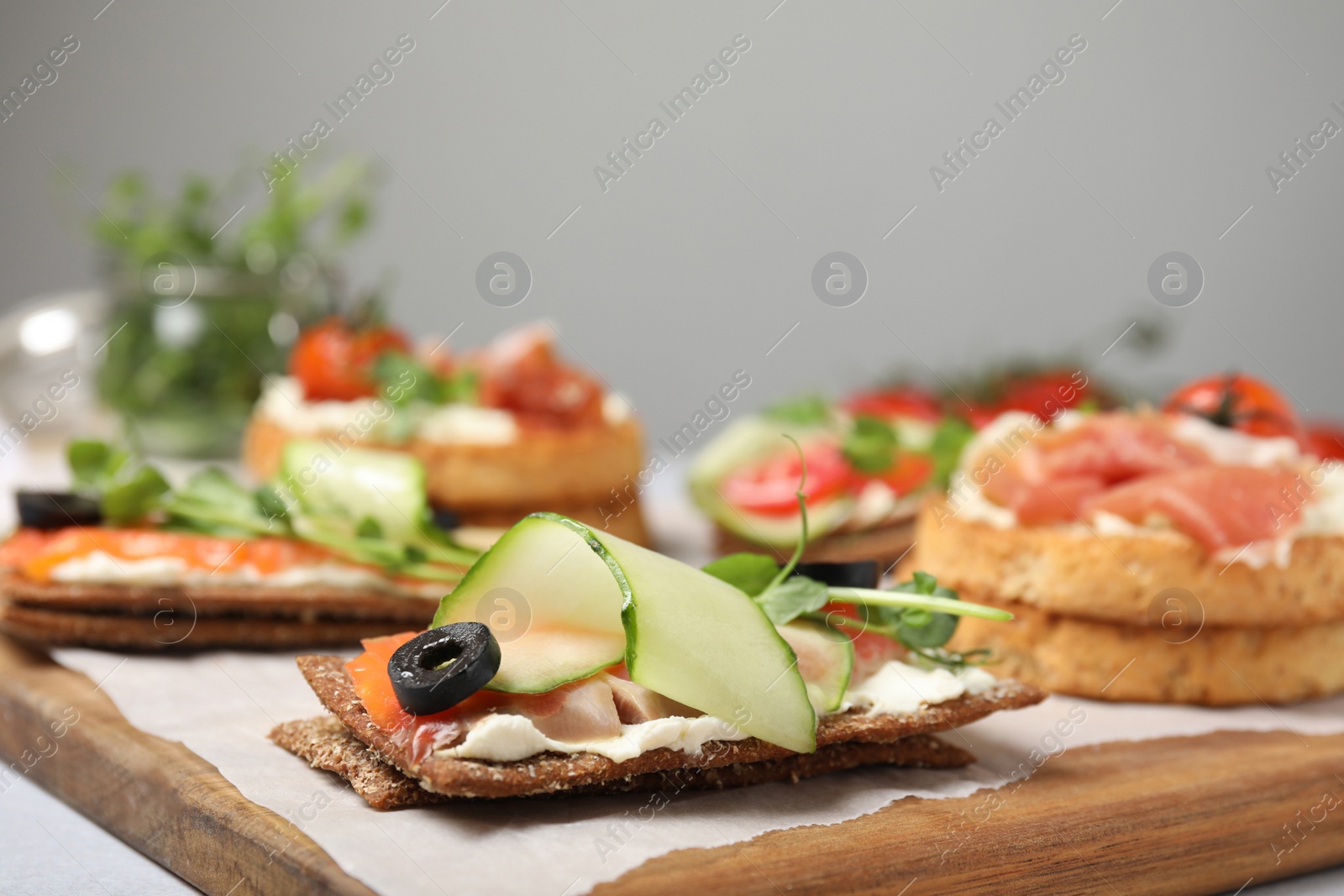 Photo of Tasty rye crispbreads with salmon, cream cheese and vegetables on wooden board. closeup