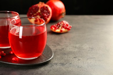 Photo of Tasty pomegranate juice in glasses and fresh fruits on grey table, closeup. Space for text