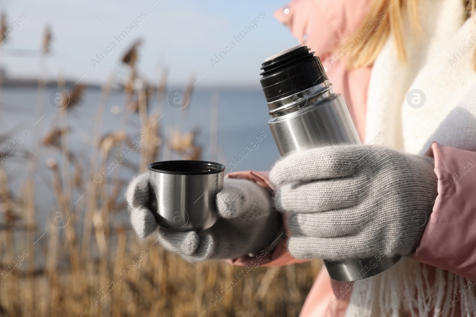 Photo of Woman pouring hot drink into cup from thermos outdoors, closeup