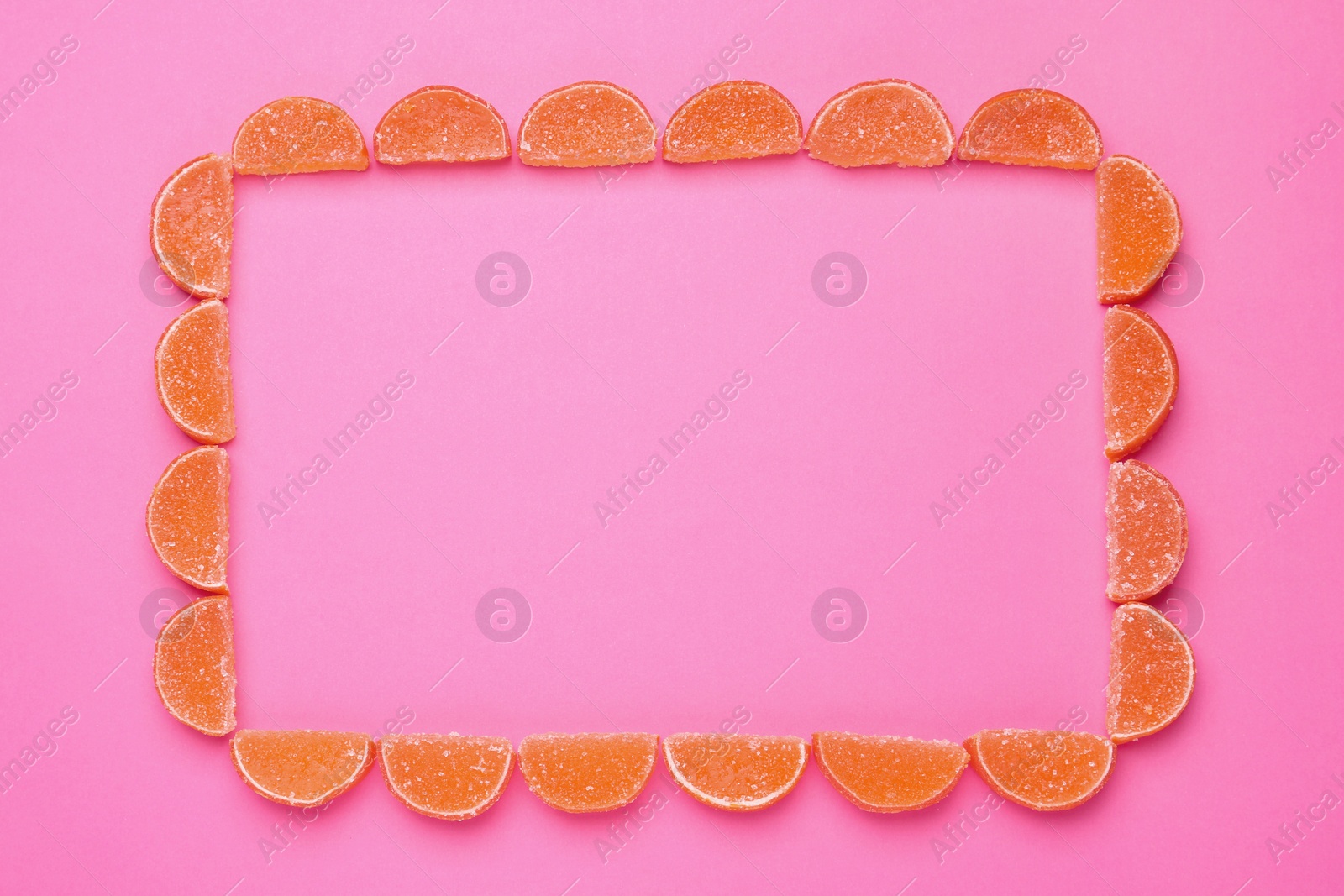 Photo of Frame made with orange marmalade candies on pink background, flat lay