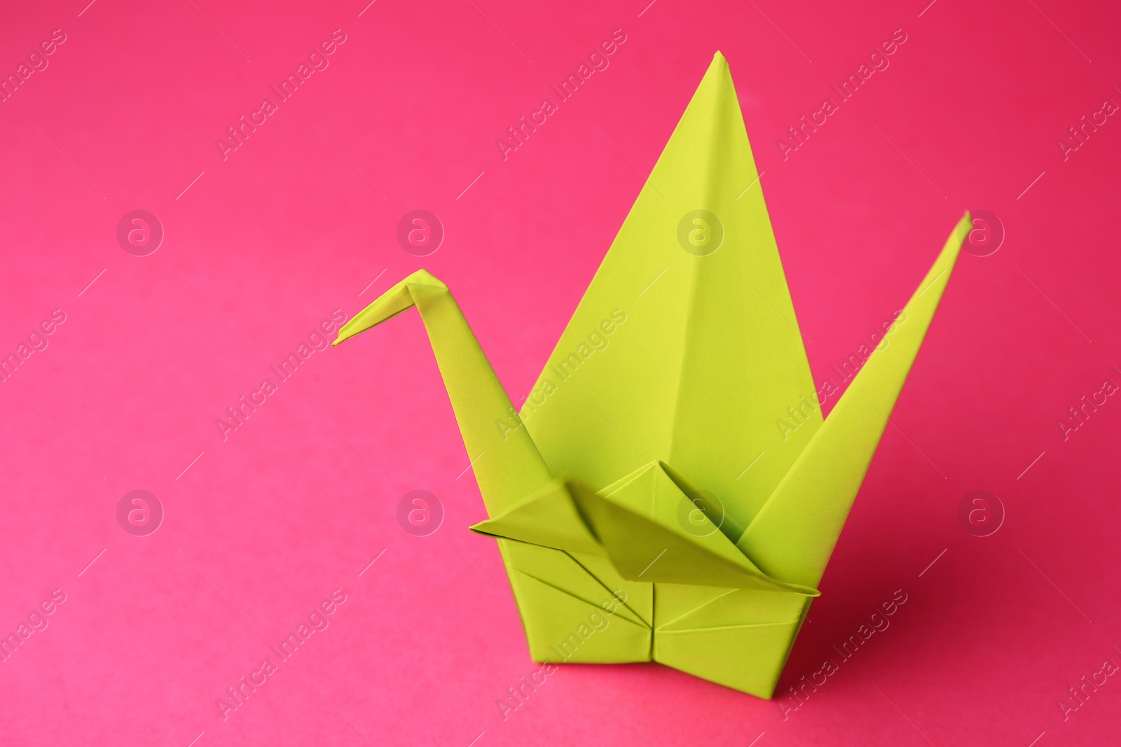 Photo of Origami art. Handmade paper crane on pink background, closeup. Space for text