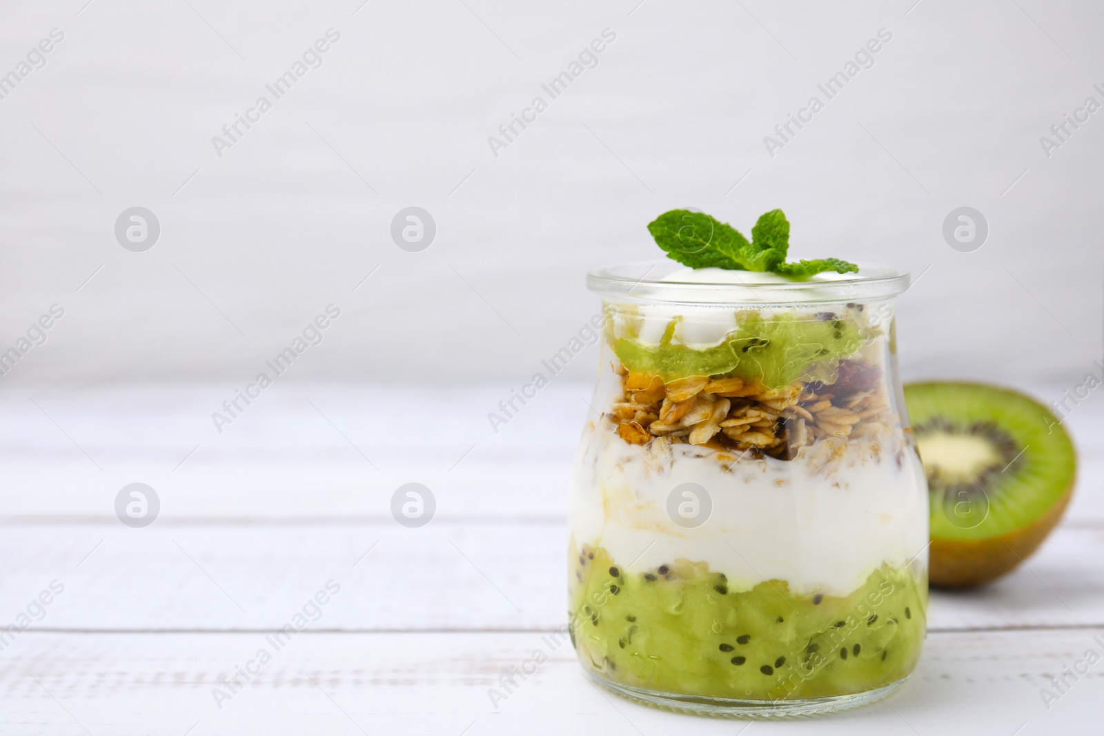 Photo of Delicious dessert with kiwi, yogurt and muesli on white wooden table, space for text