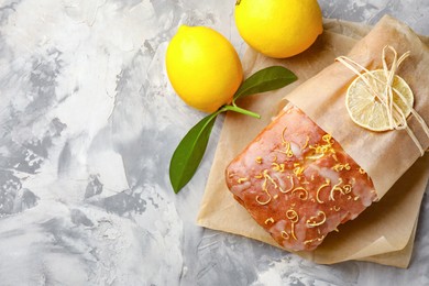Photo of Wrapped tasty lemon cake with glaze and citrus fruits on light grey textured table, top view. Space for text
