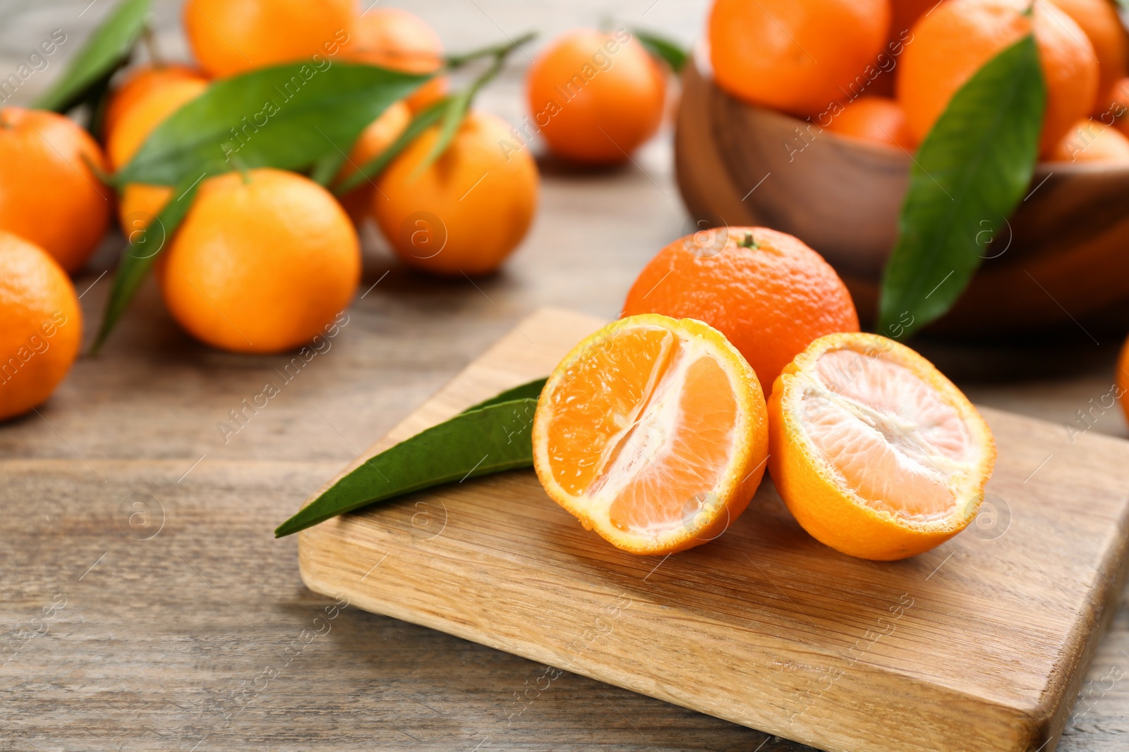 Photo of Fresh ripe tangerines with green leaves on wooden table