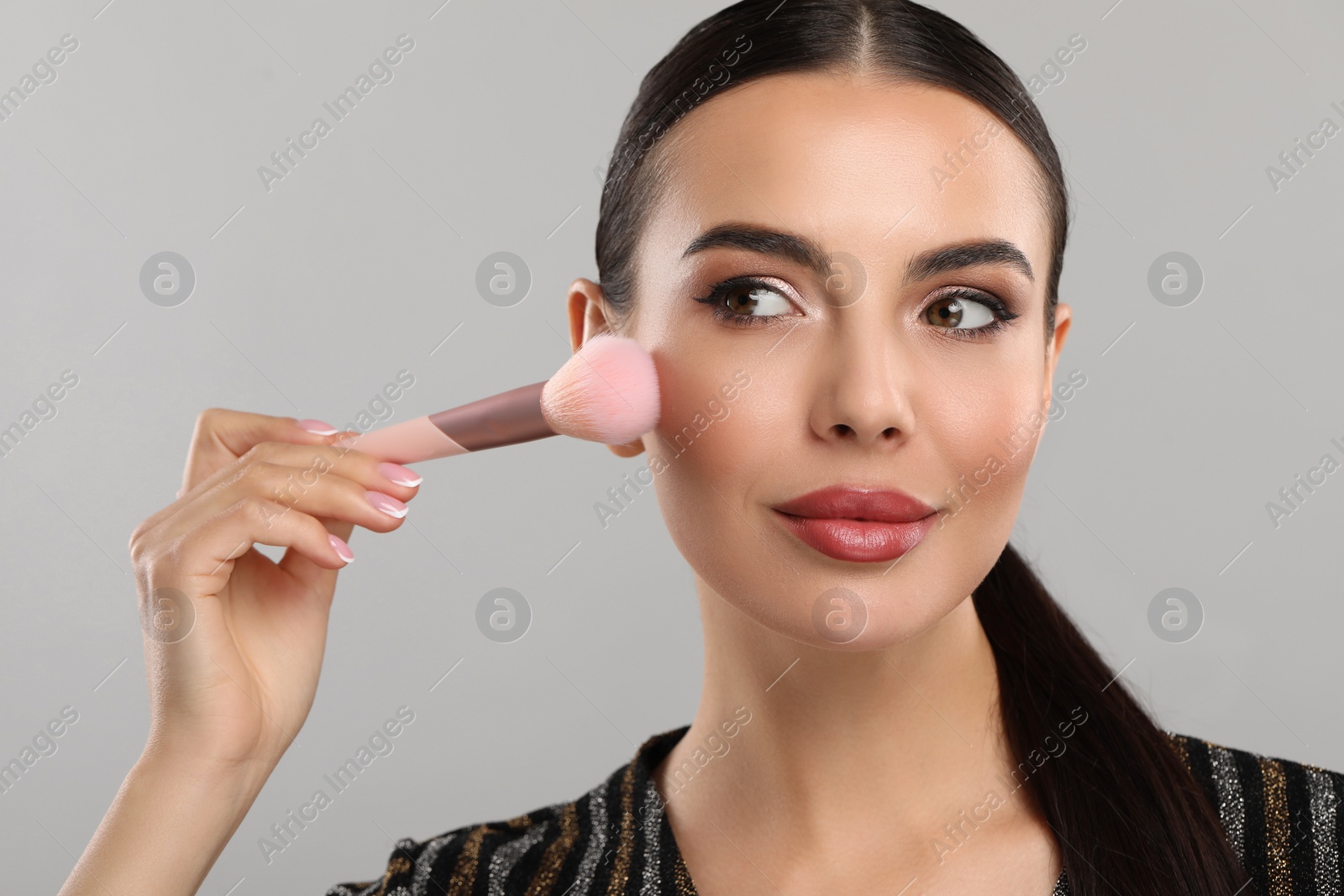 Photo of Everyday makeup. Beautiful woman applying face powder on light grey background