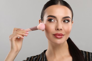 Everyday makeup. Beautiful woman applying face powder on light grey background