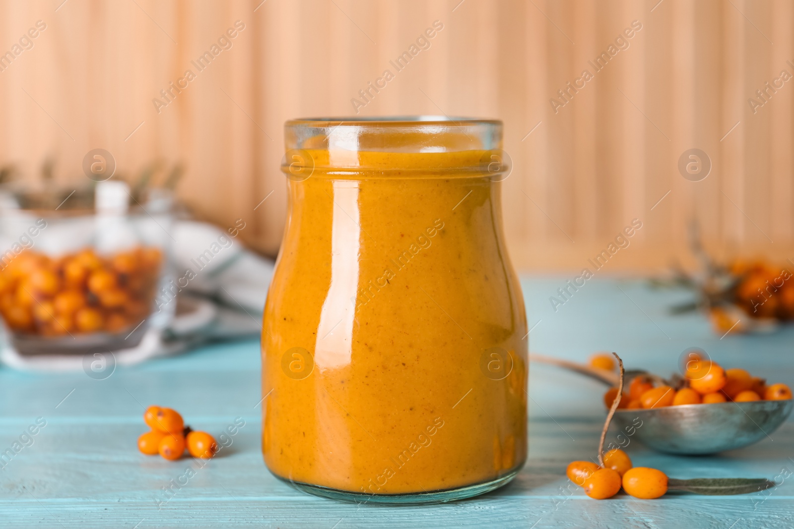 Photo of Delicious sea buckthorn jam and fresh berries on light blue wooden table