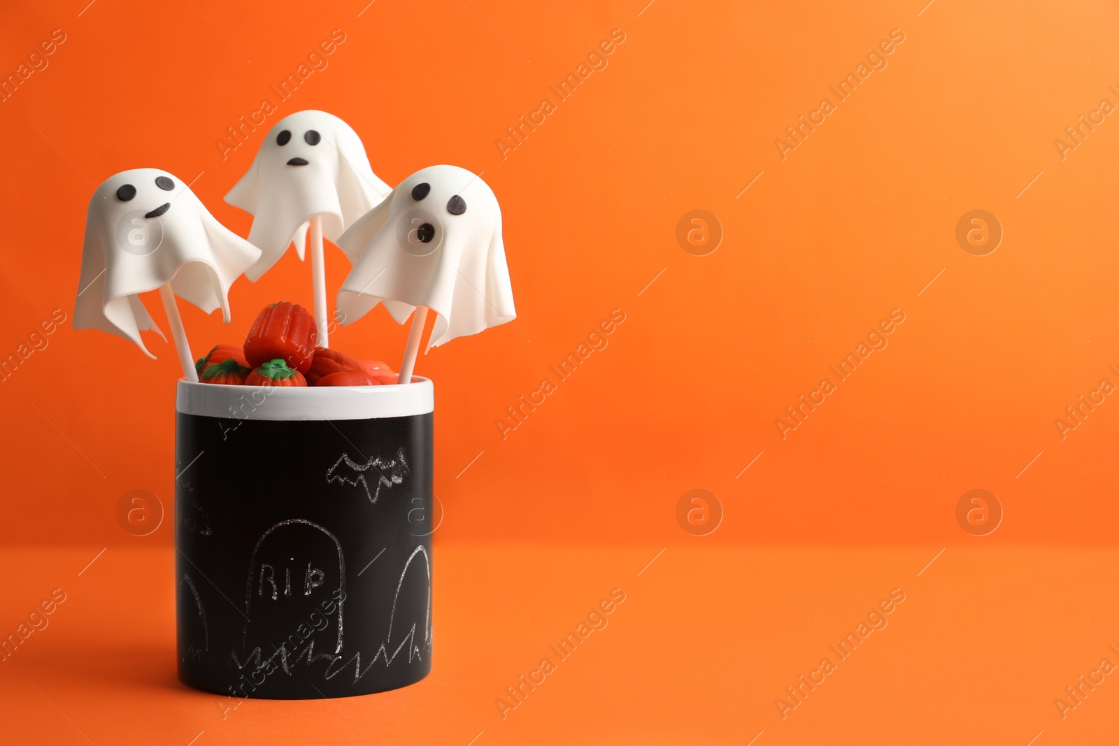 Photo of Delicious ghost shaped cake pops on orange background, space for text. Halloween celebration
