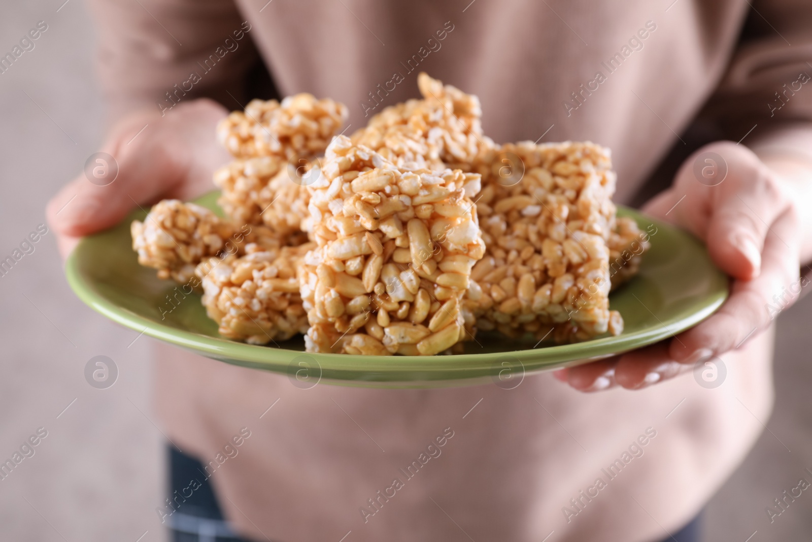 Photo of Woman holding plate with puffed rice pieces (kozinaki), closeup
