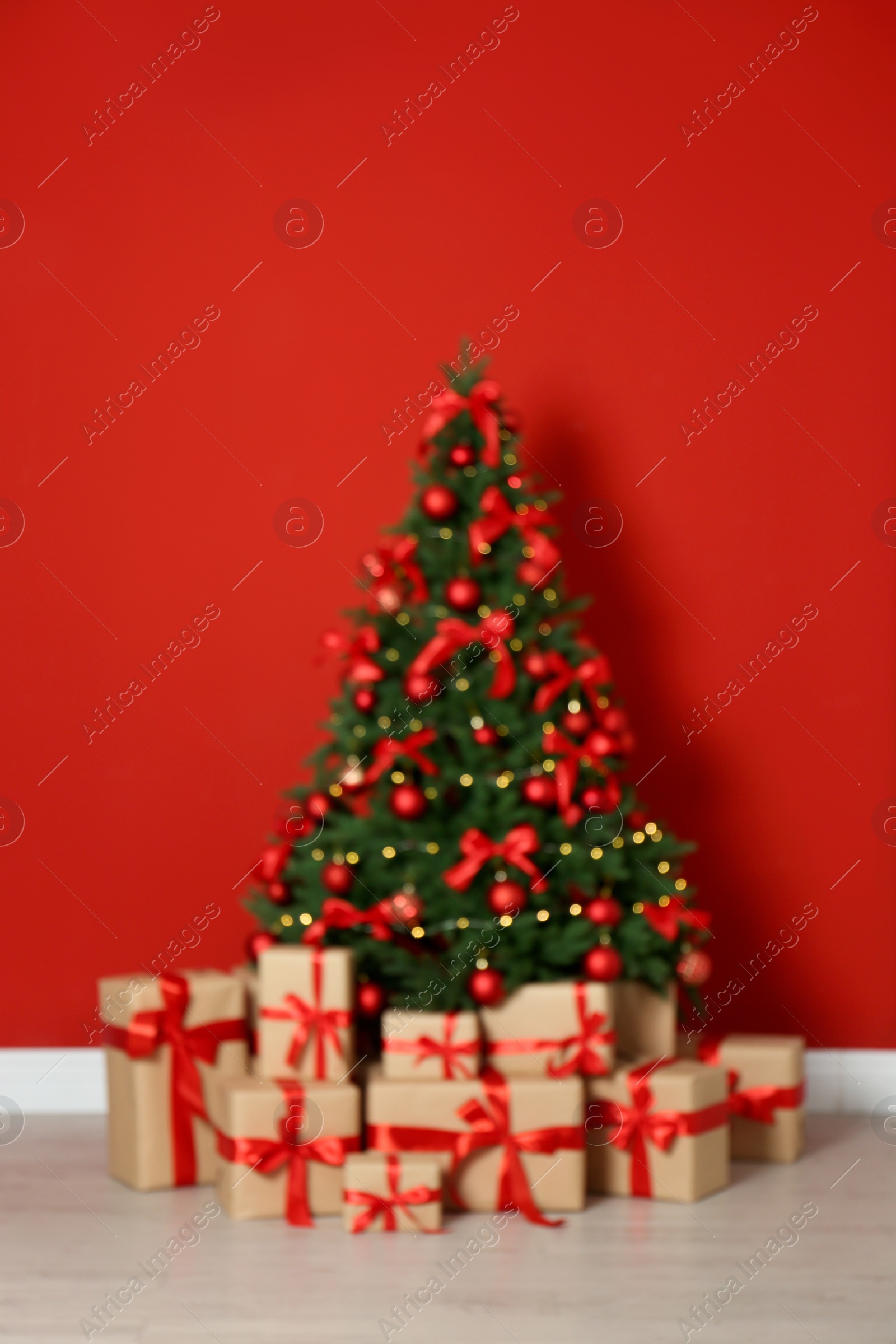 Photo of Blurred view of decorated Christmas tree and gift boxes near red wall