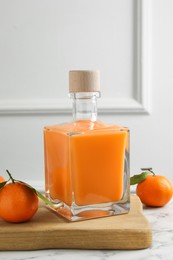 Photo of Delicious tangerine liqueur in bottle and fresh fruits on white marble table