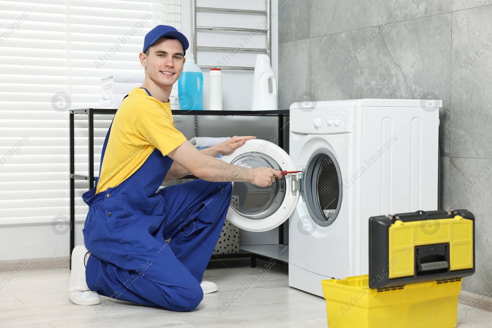 Photo of Smiling plumber repairing washing machine in bathroom