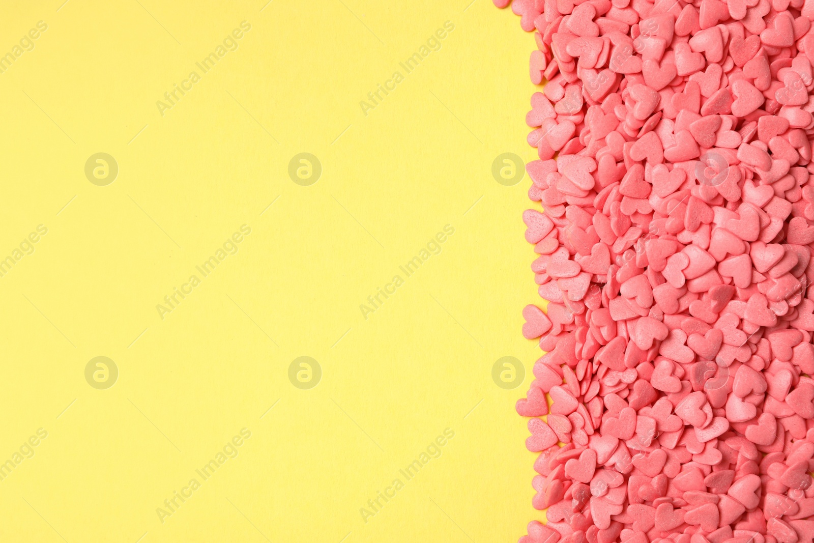 Photo of Bright heart shaped sprinkles on yellow background, flat lay. Space for text