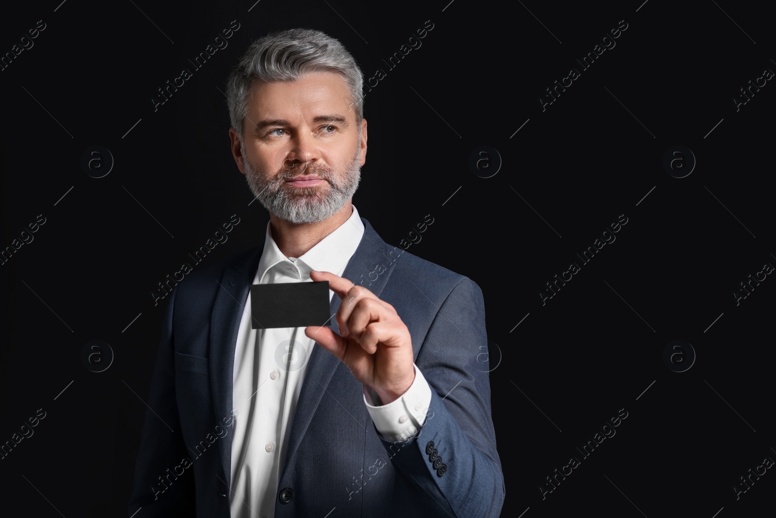 Photo of Handsome businessman holding blank business card on black background. Space for text