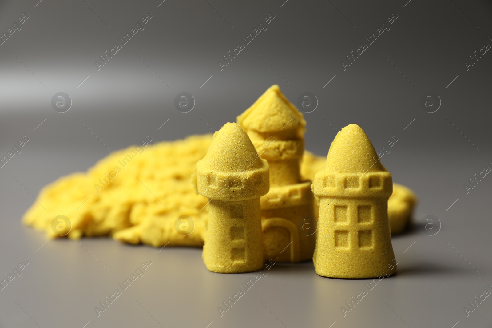 Photo of Castle figures made of yellow kinetic sand on grey background, closeup. Space for text