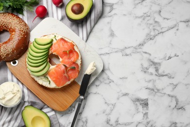 Delicious bagel with cream cheese, salmon and avocado on white marble table, flat lay. Space for text