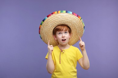 Photo of Surprised boy in Mexican sombrero hat pointing at something on violet background