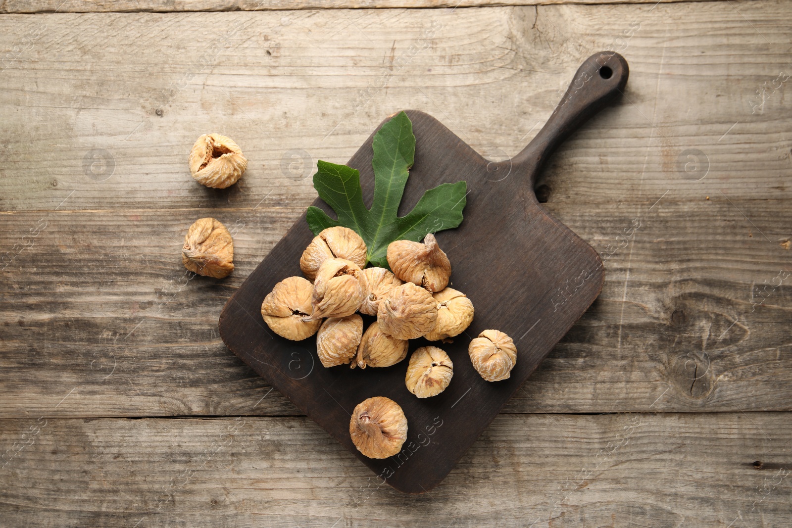 Photo of Board with tasty dried figs and green leaf on wooden table, flat lay