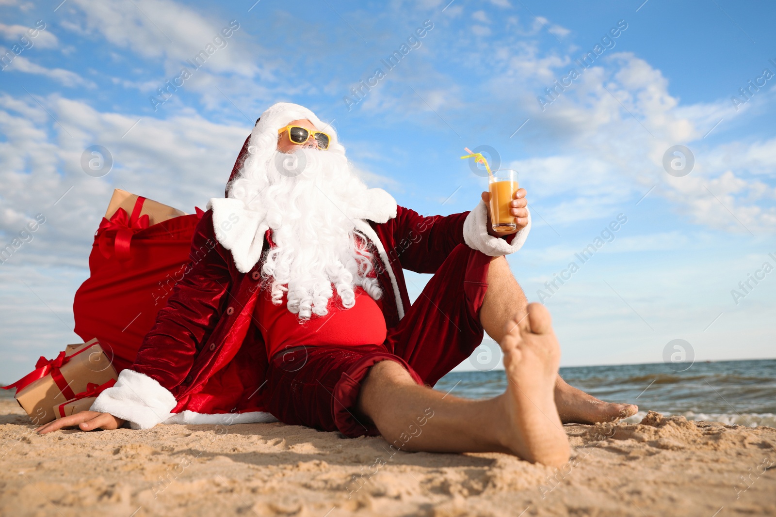 Photo of Santa Claus with cocktail relaxing on beach. Christmas vacation