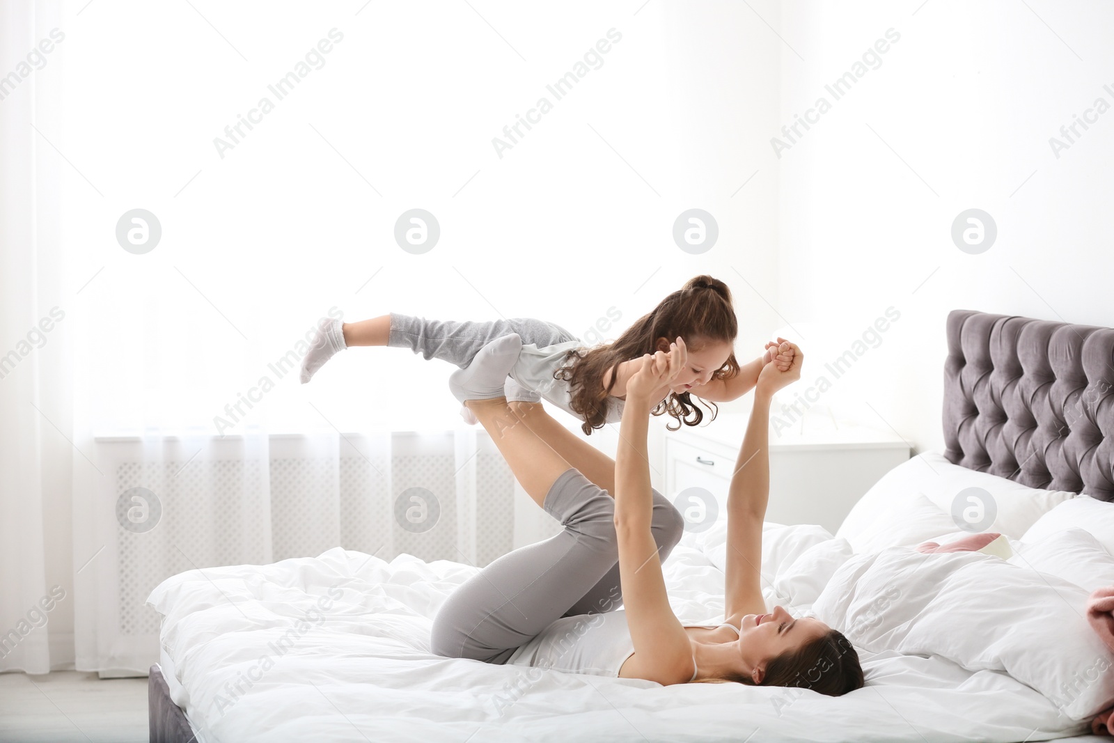 Photo of Happy mother with little daughter playing on bed