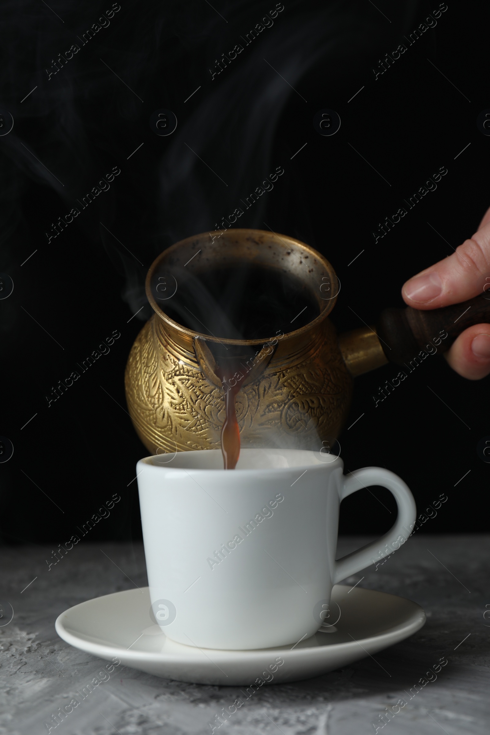 Photo of Turkish coffee. Woman pouring brewed beverage from cezve into cup at grey table, closeup