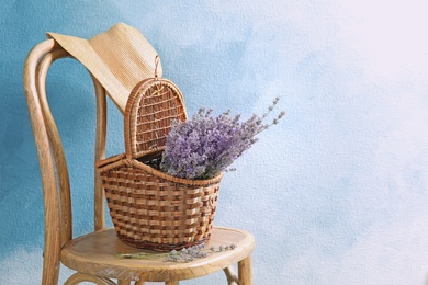 Wicker basket with lavender flowers on chair against color background