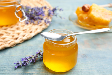 Photo of Tasty honey in glass jar and lavender flowers on light blue wooden table