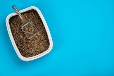 Photo of Cat litter tray with filler and scoop on light blue background, top view. Space for text