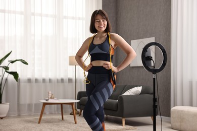 Happy sports blogger with skipping rope streaming online fitness lesson with smartphone at home