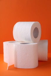 Photo of Soft toilet paper rolls on orange background, closeup