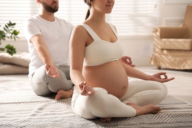 Photo of Young pregnant woman with her husband practicing yoga at home, closeup