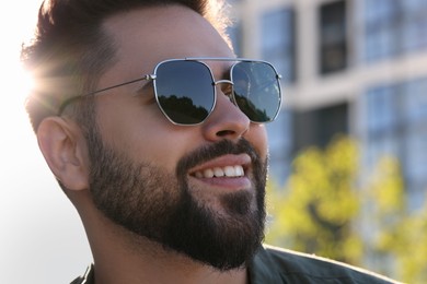 Photo of Handsome smiling man in sunglasses outdoors, closeup. Space for text