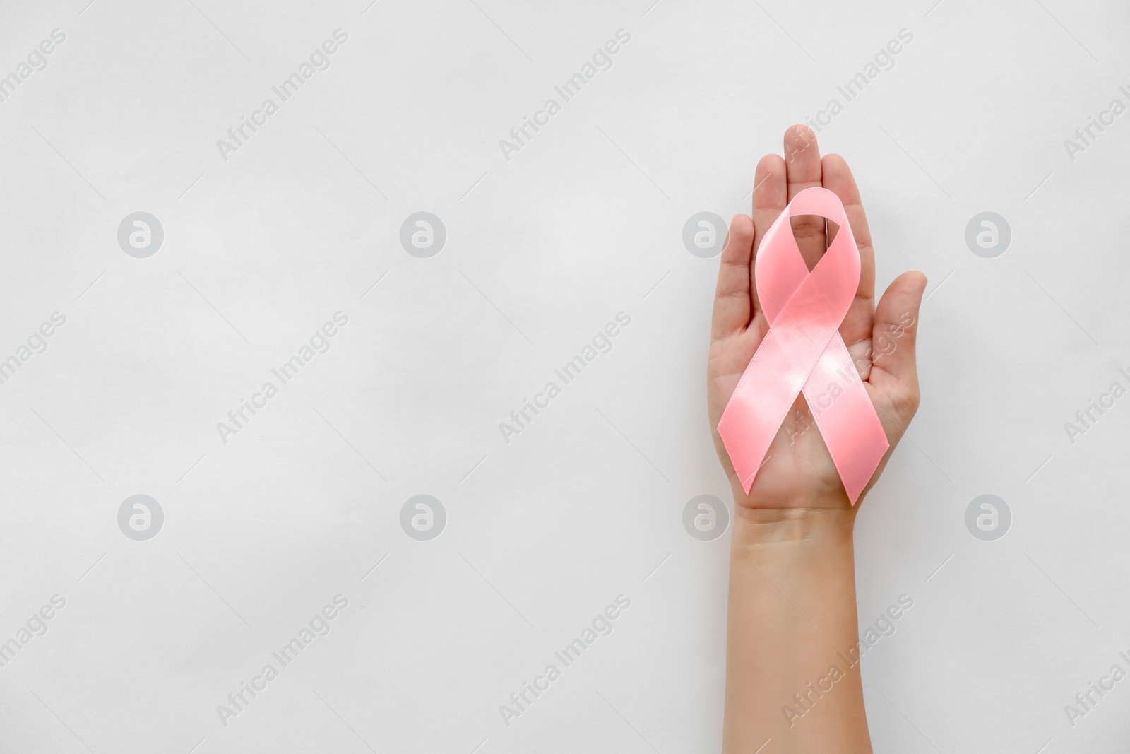 Photo of Woman holding symbolic ribbon of breast cancer awareness on light background, top view. Gynecological care