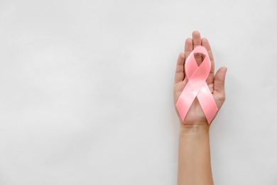 Woman holding symbolic ribbon of breast cancer awareness on light background, top view. Gynecological care