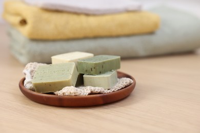 Tray with soap bars on light wooden table, space for text. Spa therapy