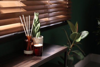 Photo of Reed freshener, candle and houseplant on table near window indoors