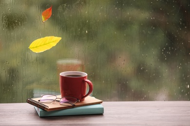 Photo of Composition with cup of drink and autumn leaf on windowsill, space for text. Rainy weather