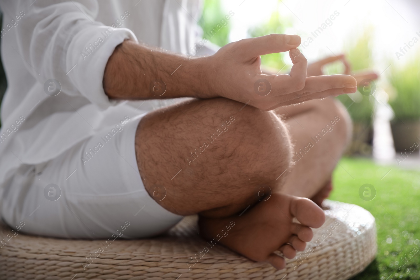 Photo of Young man meditating on straw cushion outdoors, closeup